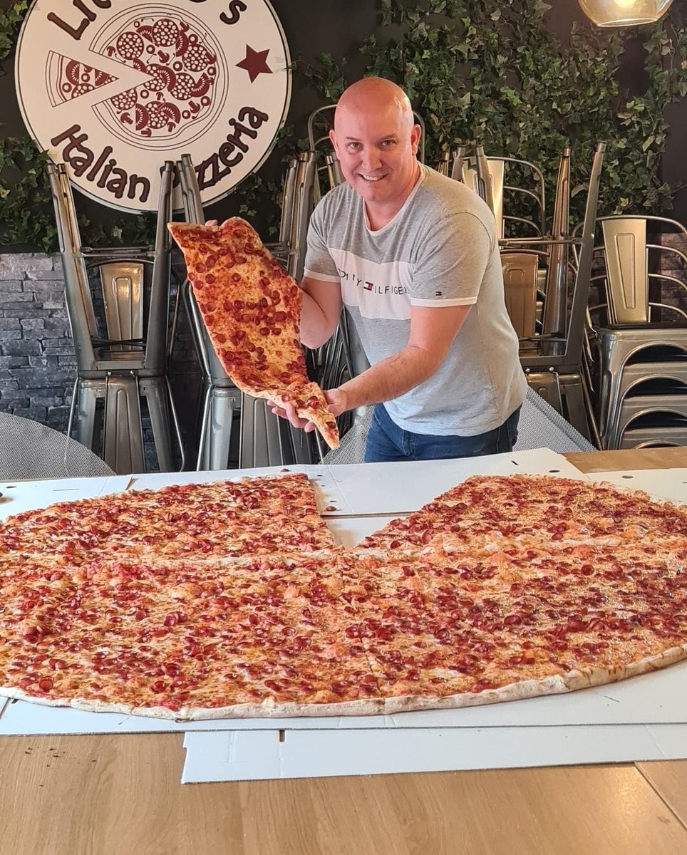 A member of the Little O's team serving a slice of a large pizza